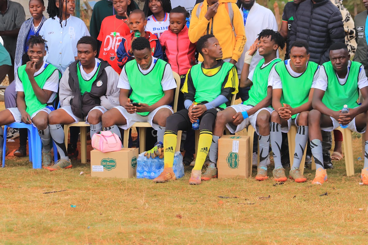 Players in green training bibs seated together beside the football pitch